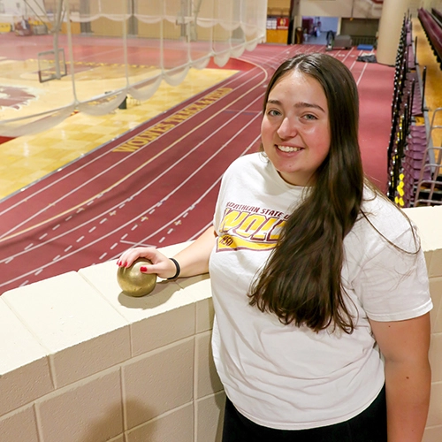 Female student standing near brick wall overlooking indoor track