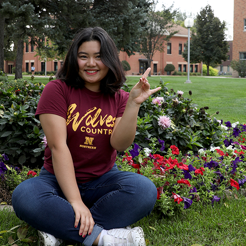 Female student sitting on grass surrounded by flowers