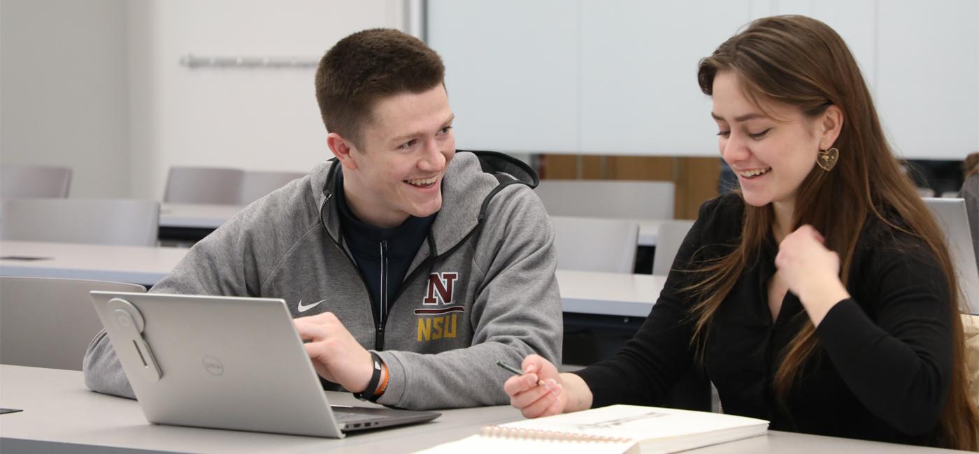 Male student with laptop and female student looking at sketch book